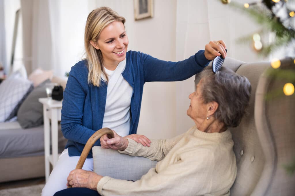 A health visitor combing hair of senior woman at home