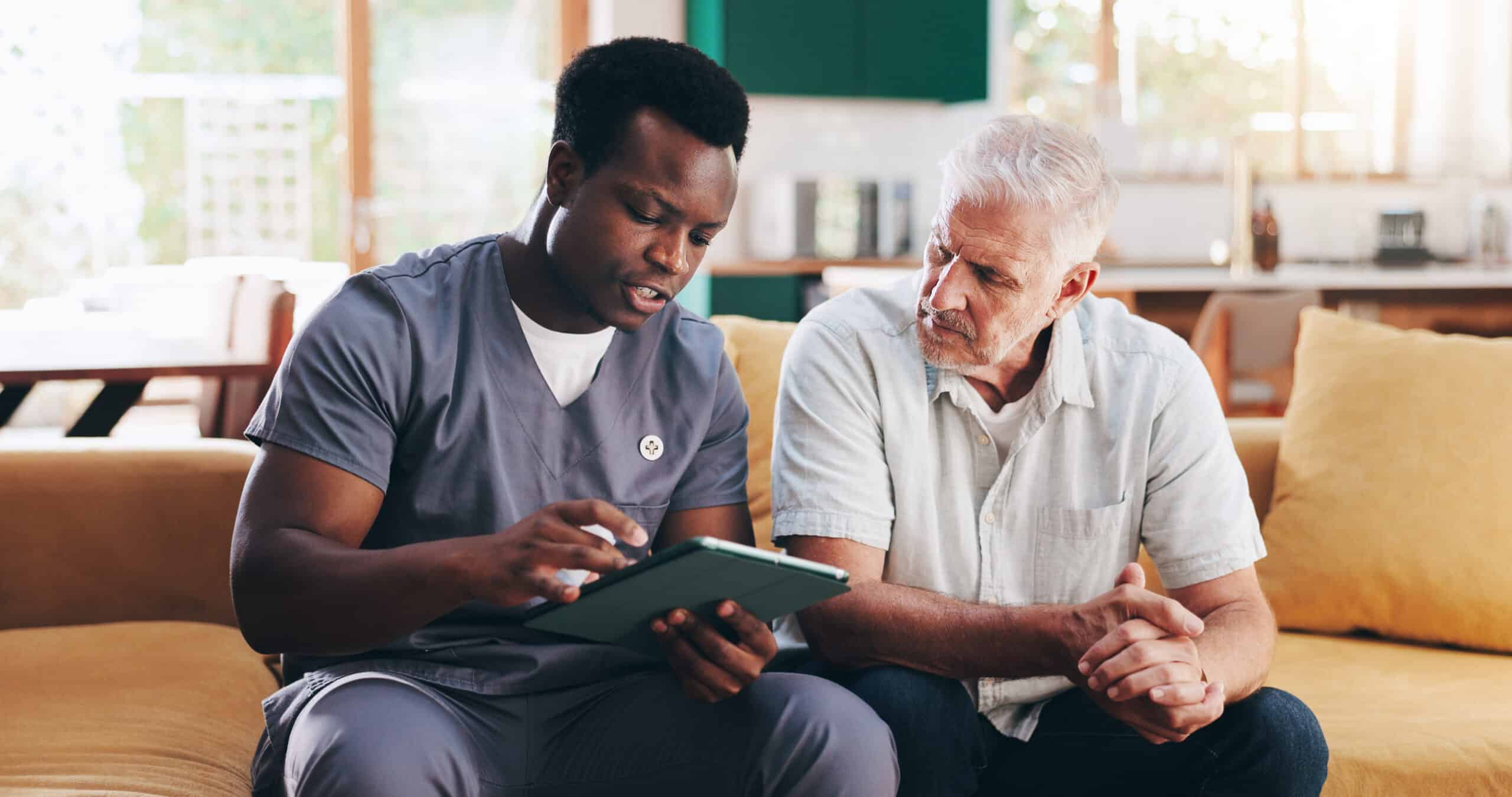 Nurse and elderly man talk on sofa